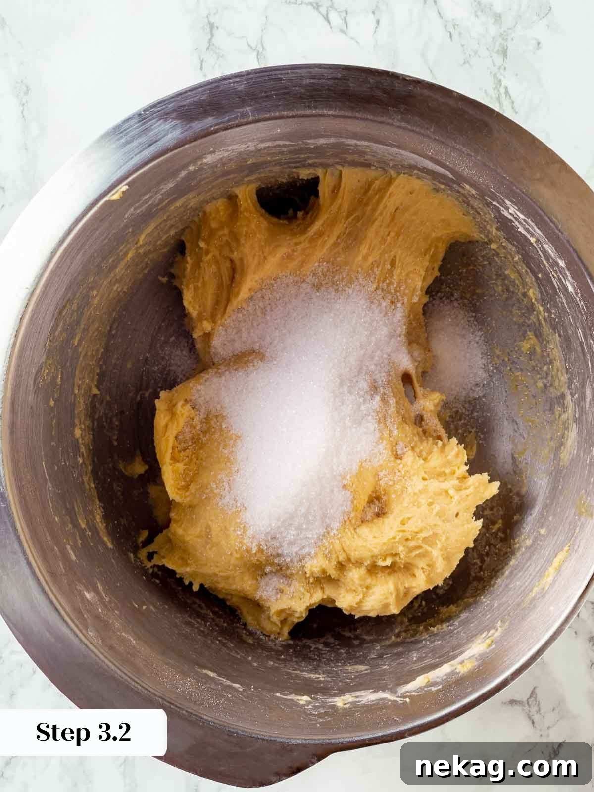Sugar being added in batches to the developing panettone dough in a stand mixer.
