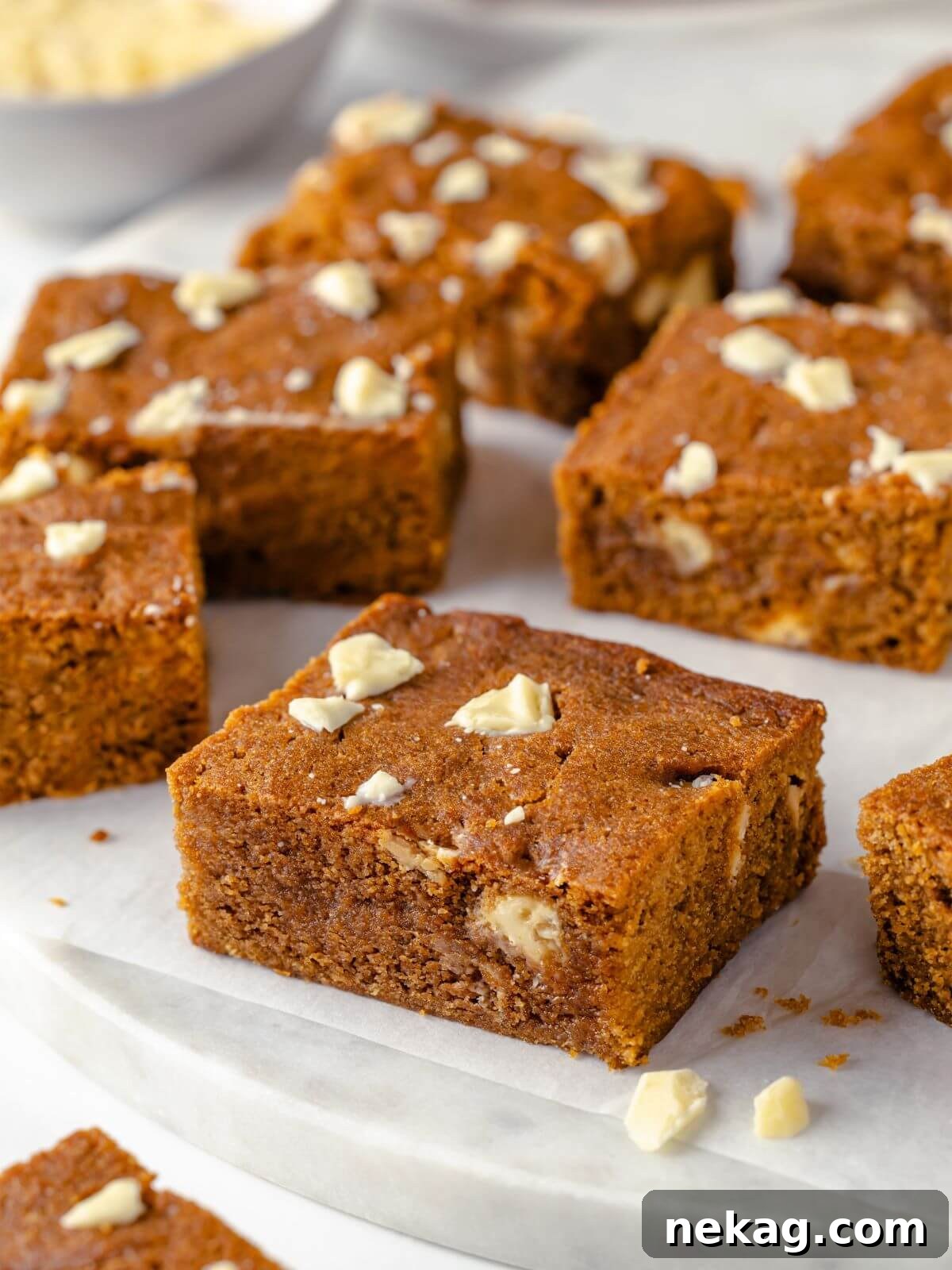 Festive Gingerbread Blondies 2 Delightfully spiced gingerbread blondies, studded with white chocolate, elegantly arranged on a white marble surface for a minimalist and inviting aesthetic.