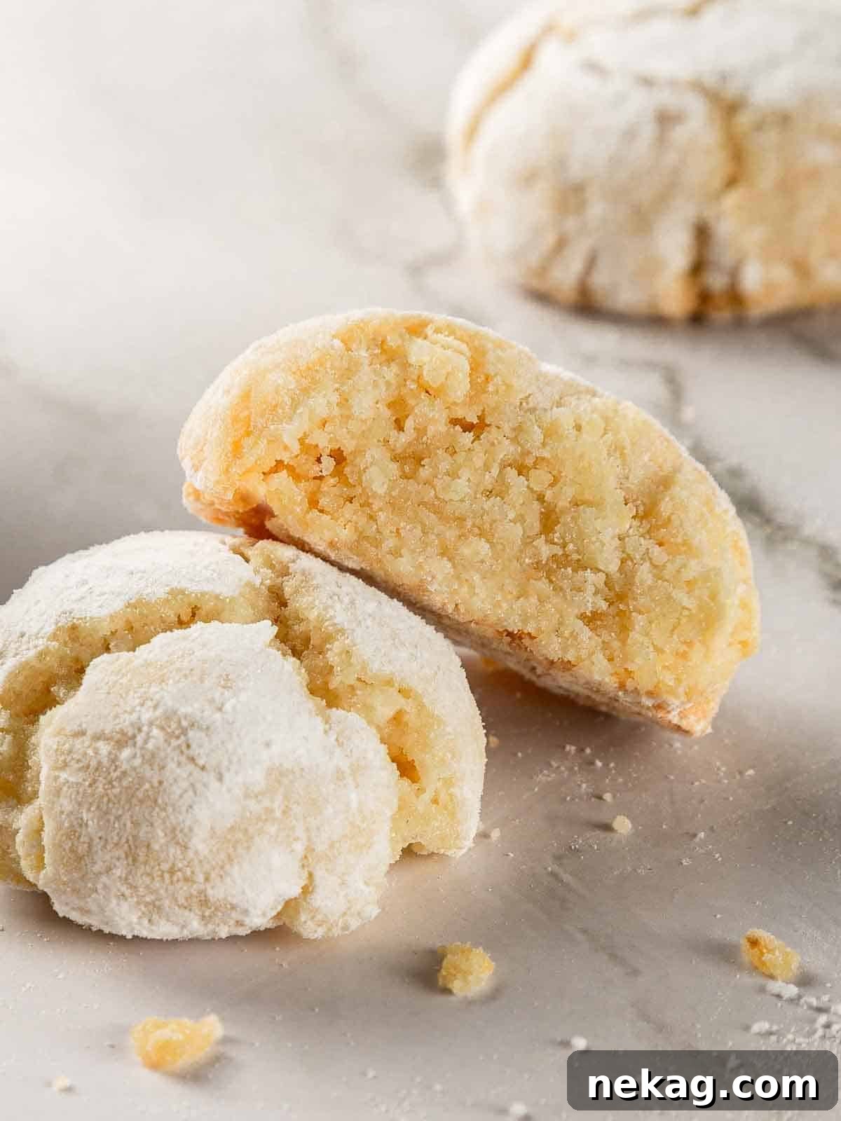 Delicate Amaretti Bites 2 Freshly baked soft amaretti cookies dusted with powdered sugar, showcasing their signature crinkled tops, on a parchment-lined baking sheet.