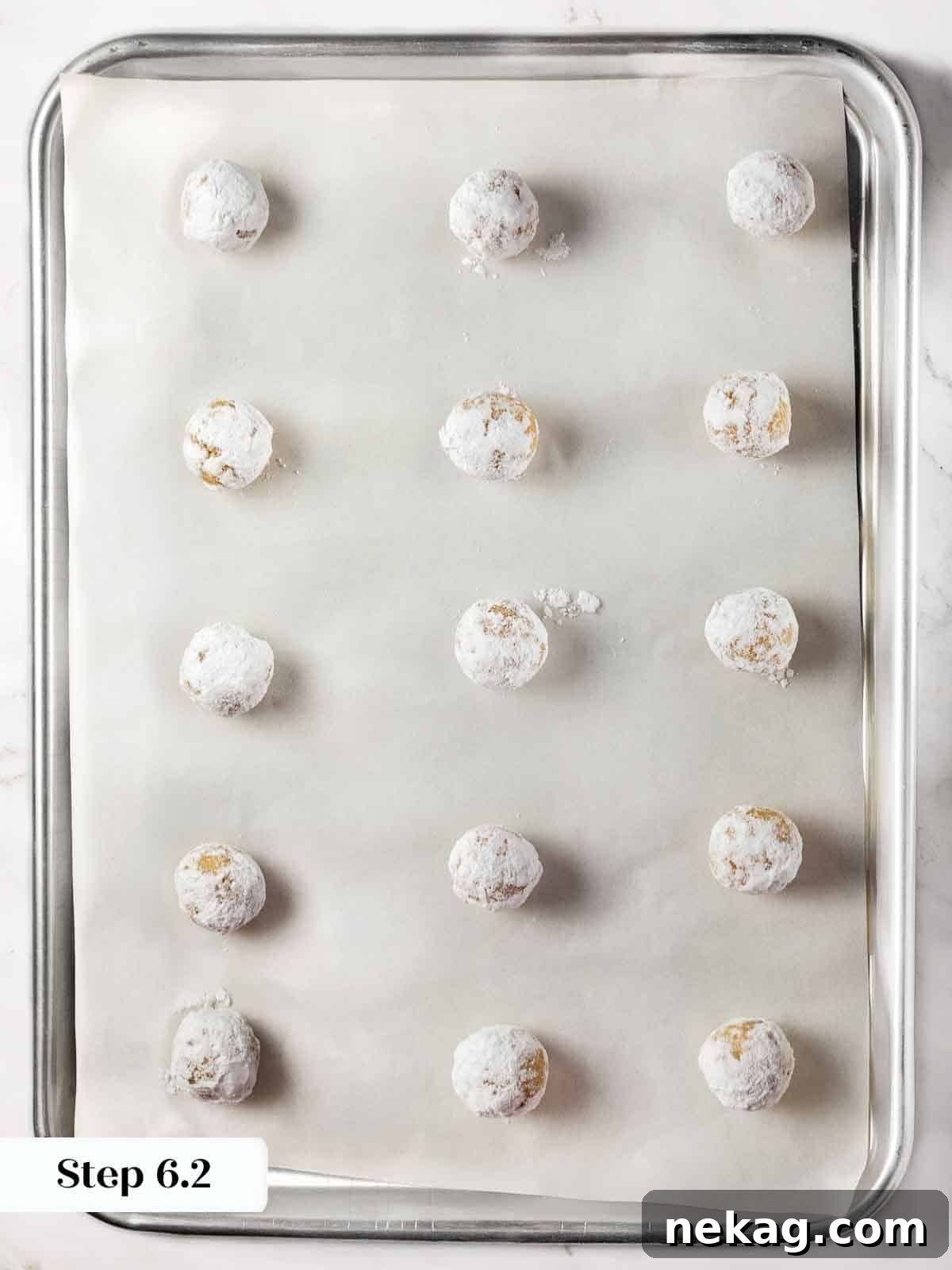 Delicate Amaretti Bites 10 Powdered sugar-coated amaretti cookie dough balls arranged on a parchment-lined baking sheet, ready for the oven.