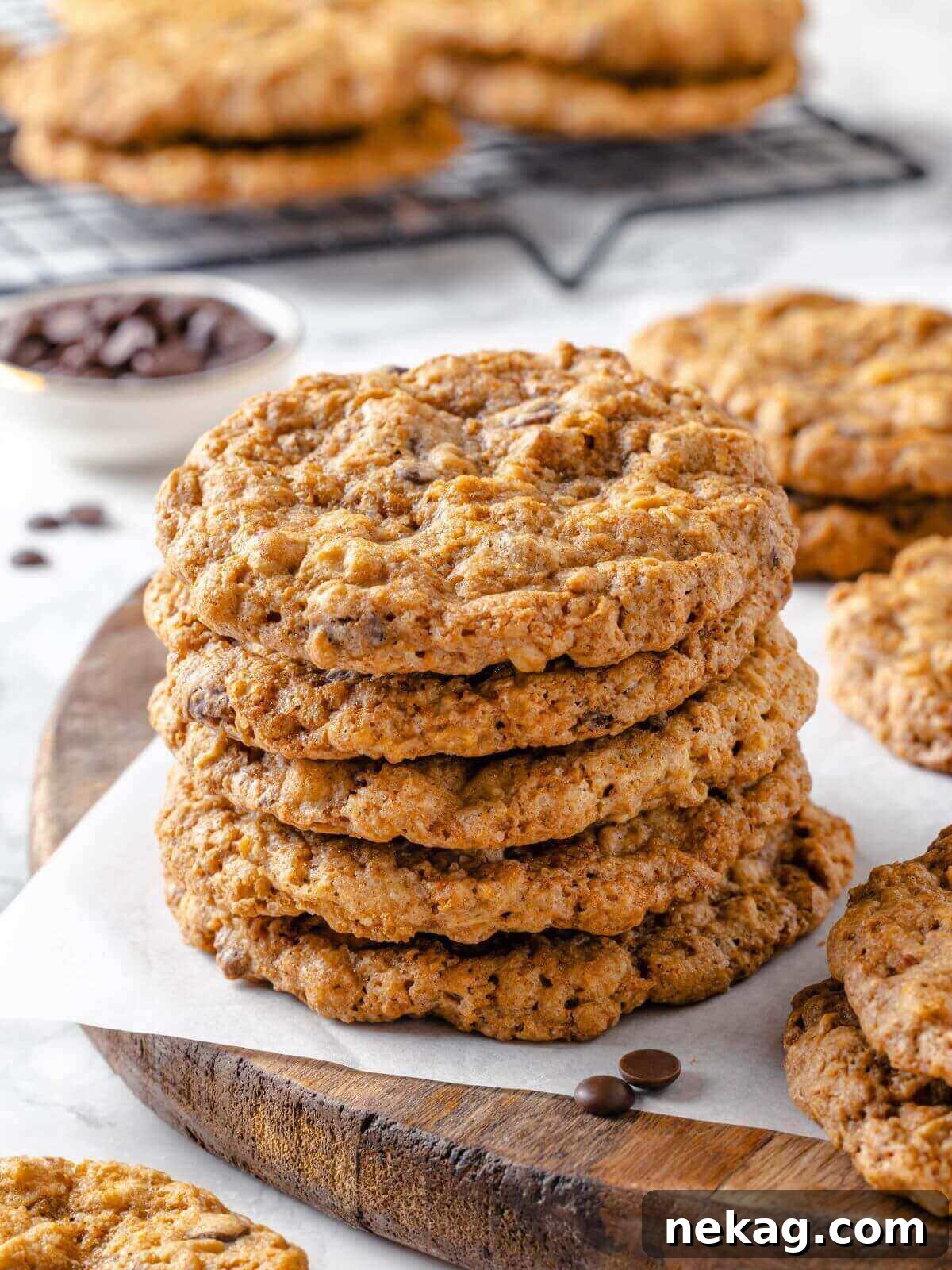 Hearty Cowboy Cookie Bake 2 A stack of golden-brown cowboy cookies on a rustic wooden board, garnished with loose chocolate chips and oats, showcasing their abundant mix-ins and inviting texture.
