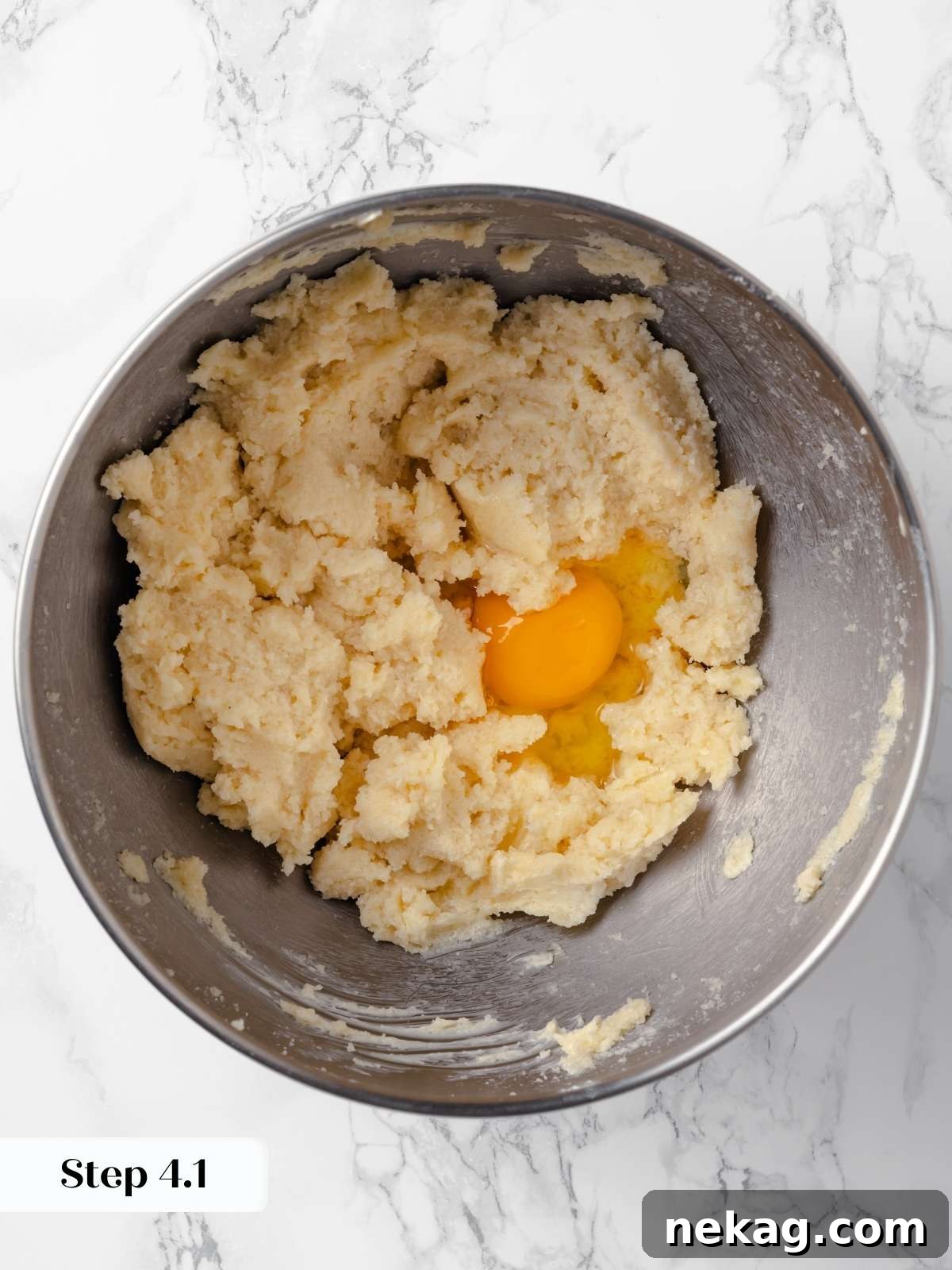 Hearty Cowboy Cookie Bake 9 Large eggs being cracked and added one by one to the creamed butter and sugar mixture in a mixing bowl for cowboy cookies, ensuring smooth incorporation.