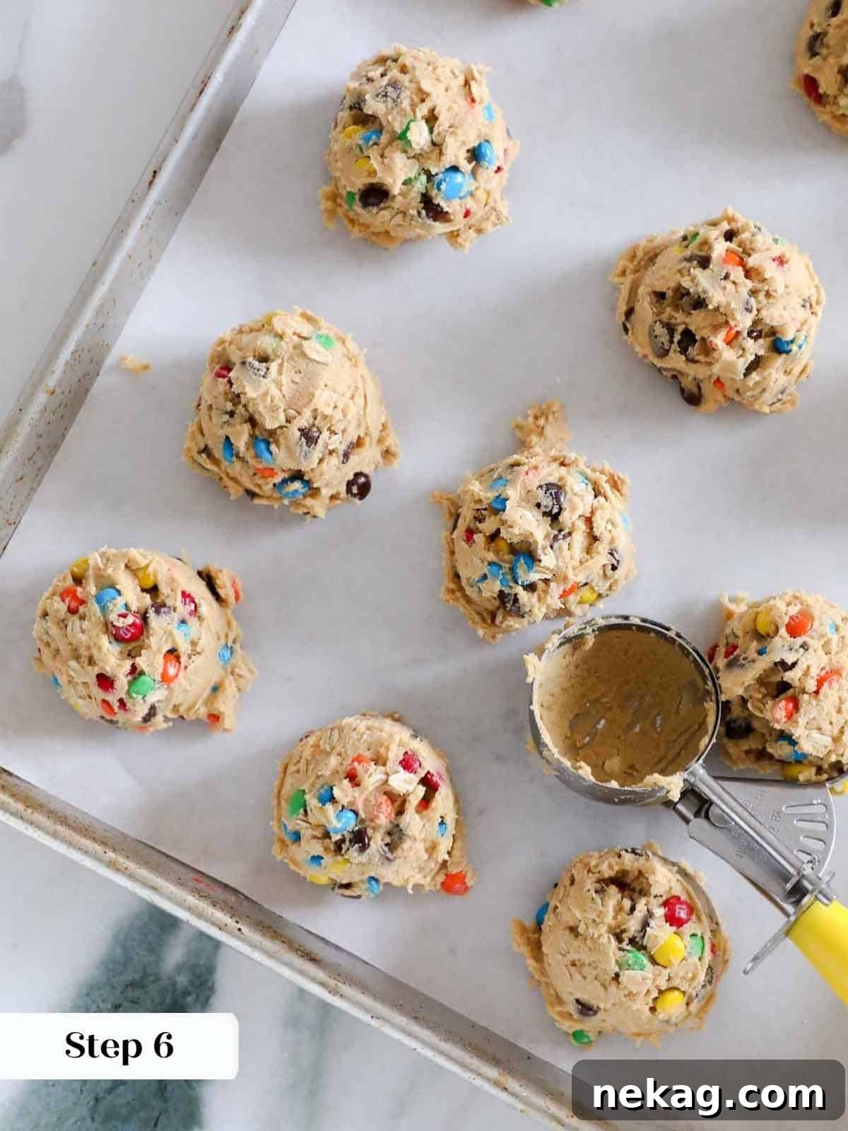 Evenly scooped portions of monster cookie dough, perfectly spaced on a parchment-lined baking sheet, ready for the oven.