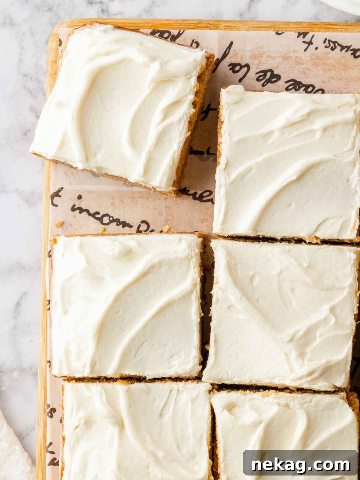 A delightful banana cake with creamy cream cheese frosting, meticulously cut into perfect squares and presented on parchment paper, ready to be served.