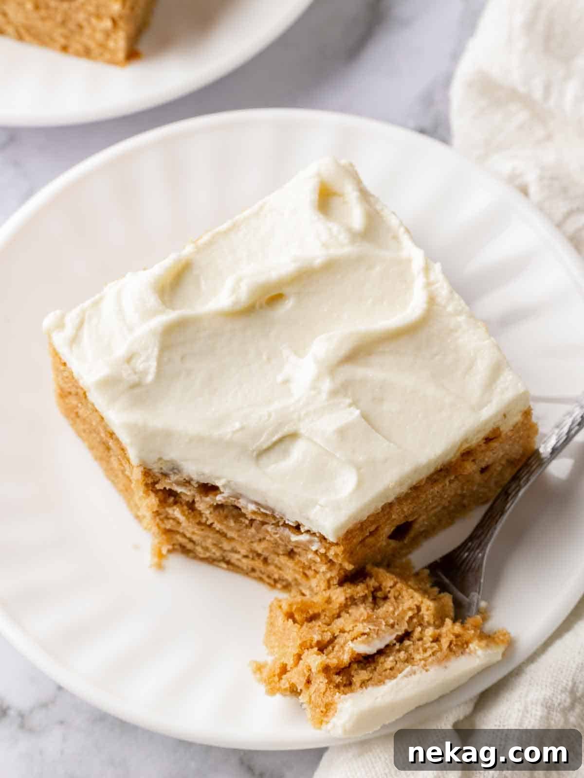 A delectable slice of moist banana cake, topped with a generous swirl of creamy cream cheese frosting, elegantly presented with a fork alongside, ready to be enjoyed.
