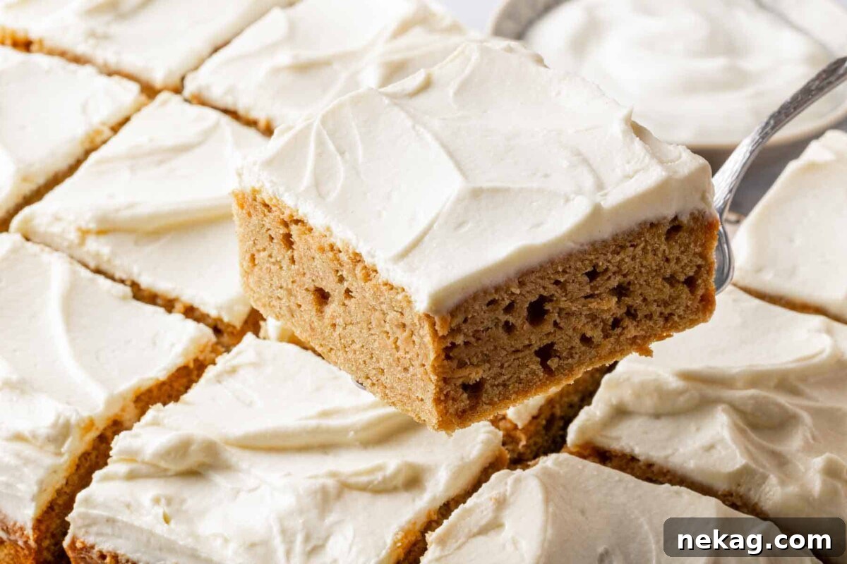 A large slice of homemade banana cake with cream cheese frosting being carefully lifted from the pan with a cake server, ready to be enjoyed.