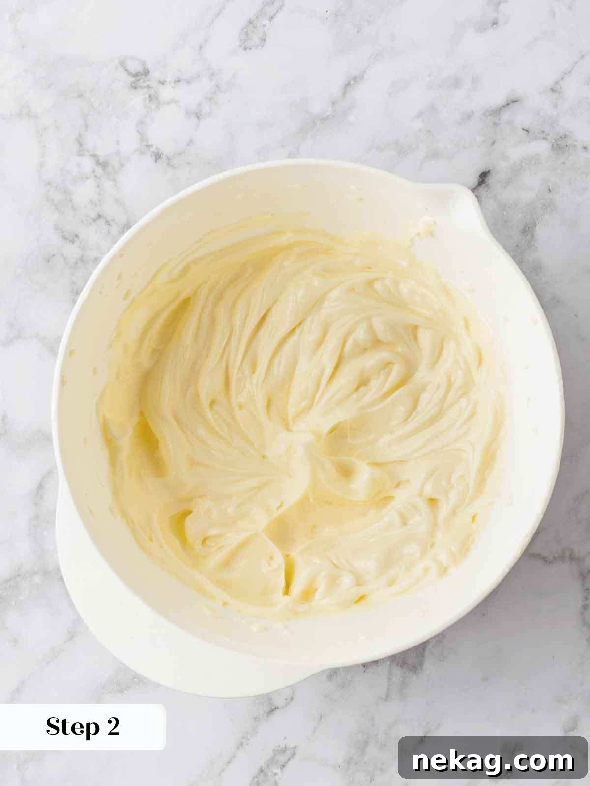 A close-up of a bowl filled with smooth, white cream cheese frosting, artfully swirled and ready to be spread over a cake or cupcakes.