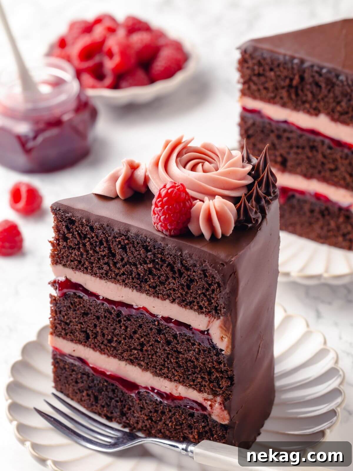 A single slice of chocolate raspberry cake showing the layered frosting and jam filling, glistening with rich chocolate and vibrant raspberry.