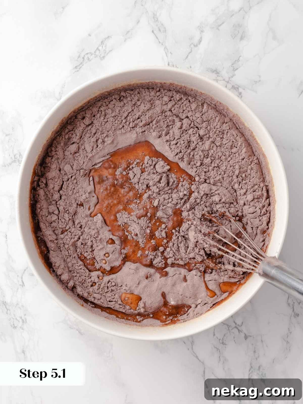 Dry ingredients being added to wet ingredients in a mixing bowl for the cake batter, showing the texture of the combined mixture.