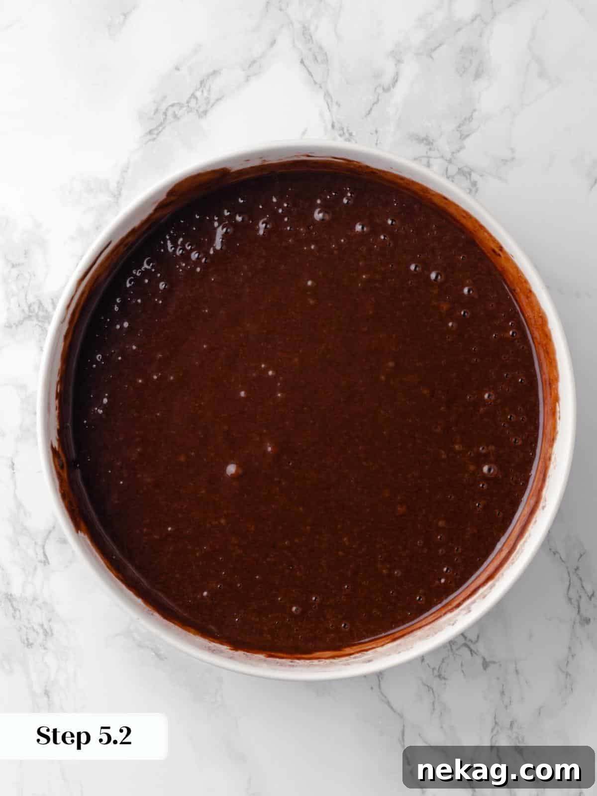 A mixing bowl filled with rich chocolate cake batter ready to be poured into pans, showcasing its smooth, glossy consistency.