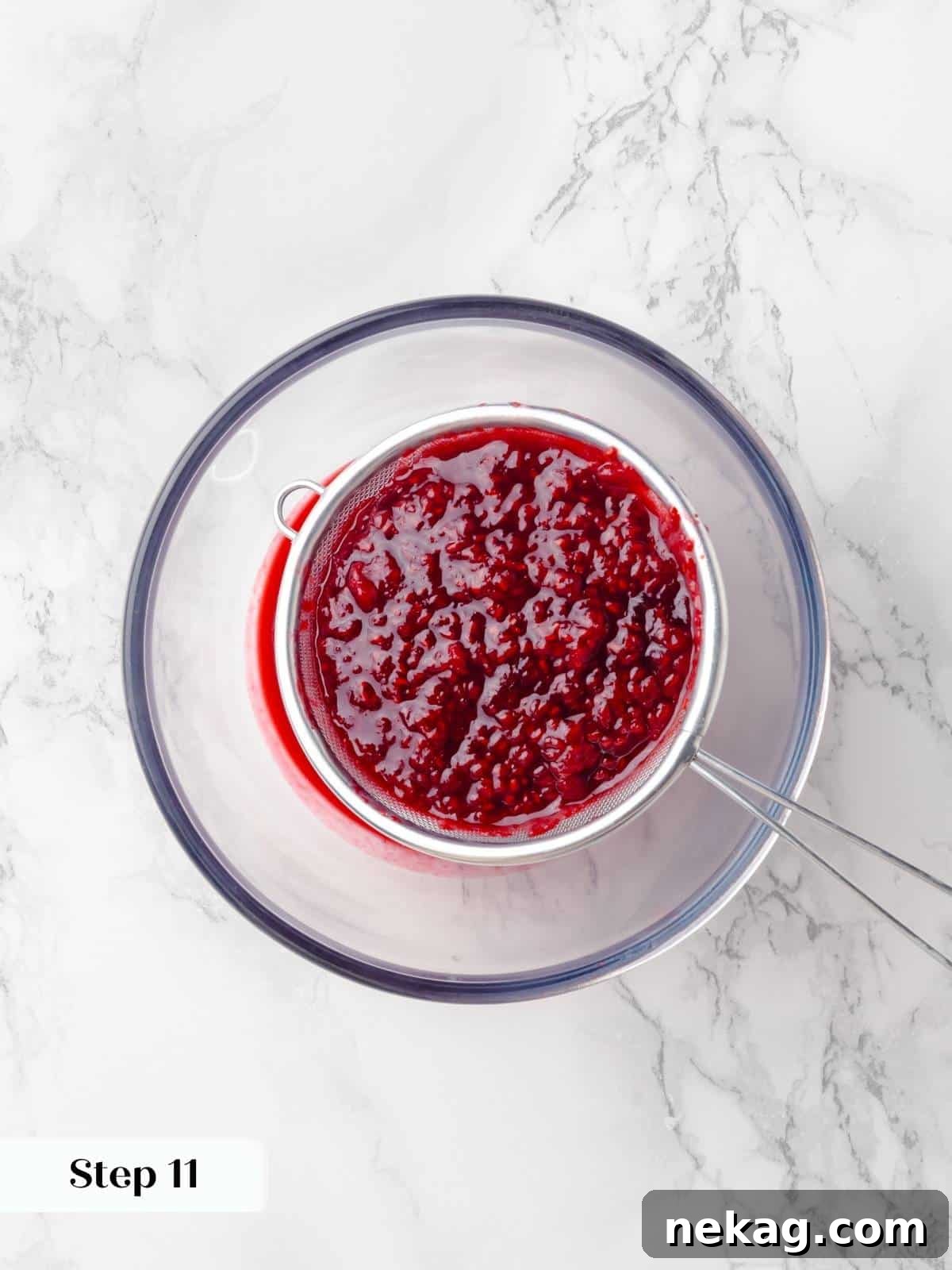 Fresh raspberries being strained through a fine-mesh sieve to remove seeds for the jam, showing the process of pressing fruit.