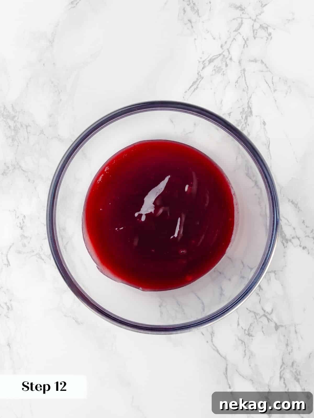 A clear bowl filled with vibrant raspberry jam, rich in color and consistency, ready to be spread onto the cake layers.