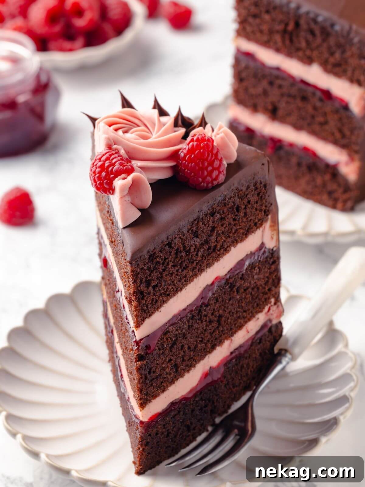 A beautifully presented slice of chocolate raspberry cake served on a pristine white plate, garnished with fresh raspberries for a touch of elegance.