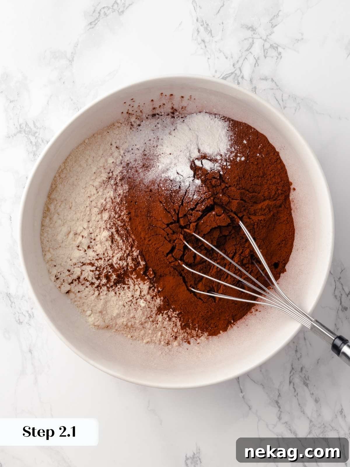 A bowl of dry ingredients being combined with a whisk for the cake batter, showing the cocoa powder and flour blend.