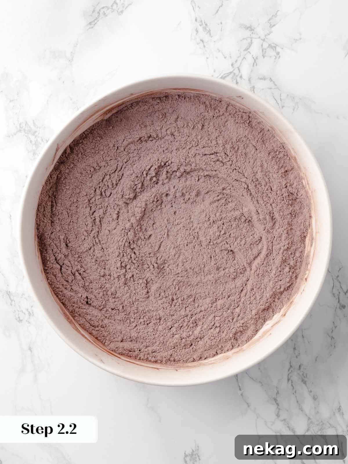 Dry ingredients for the cake, including cocoa powder and flour, mixed together in a bowl, creating a dark, even blend.