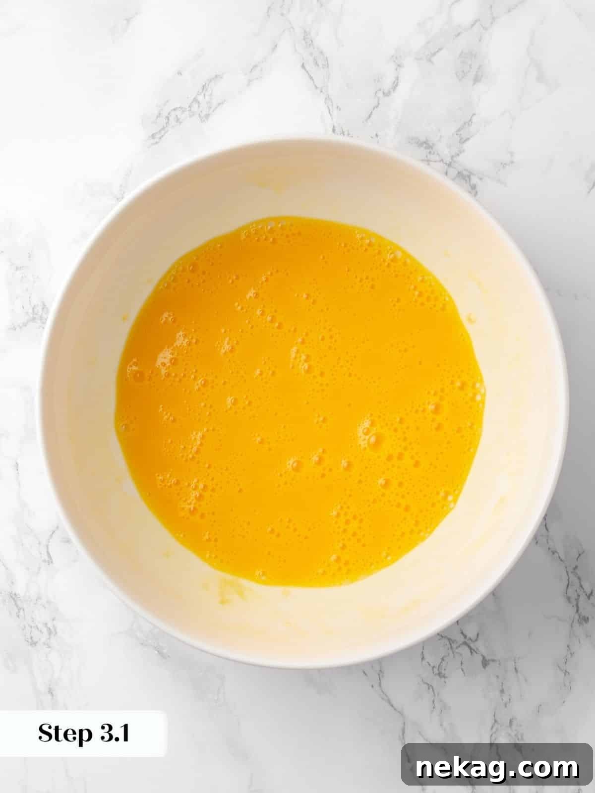 Eggs being whisked with vanilla extract in a bowl for the cake batter, showing a smooth, yellow consistency.