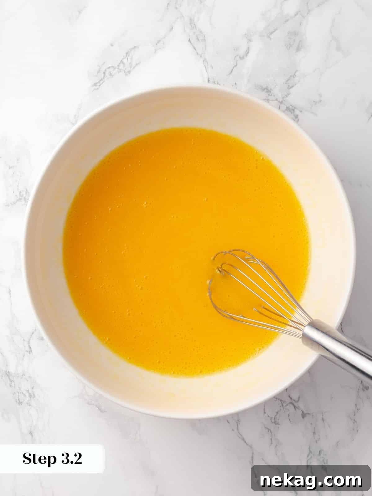 A whisk mixing eggs with oil in a glass bowl for a smooth cake batter, showing the emulsification process.