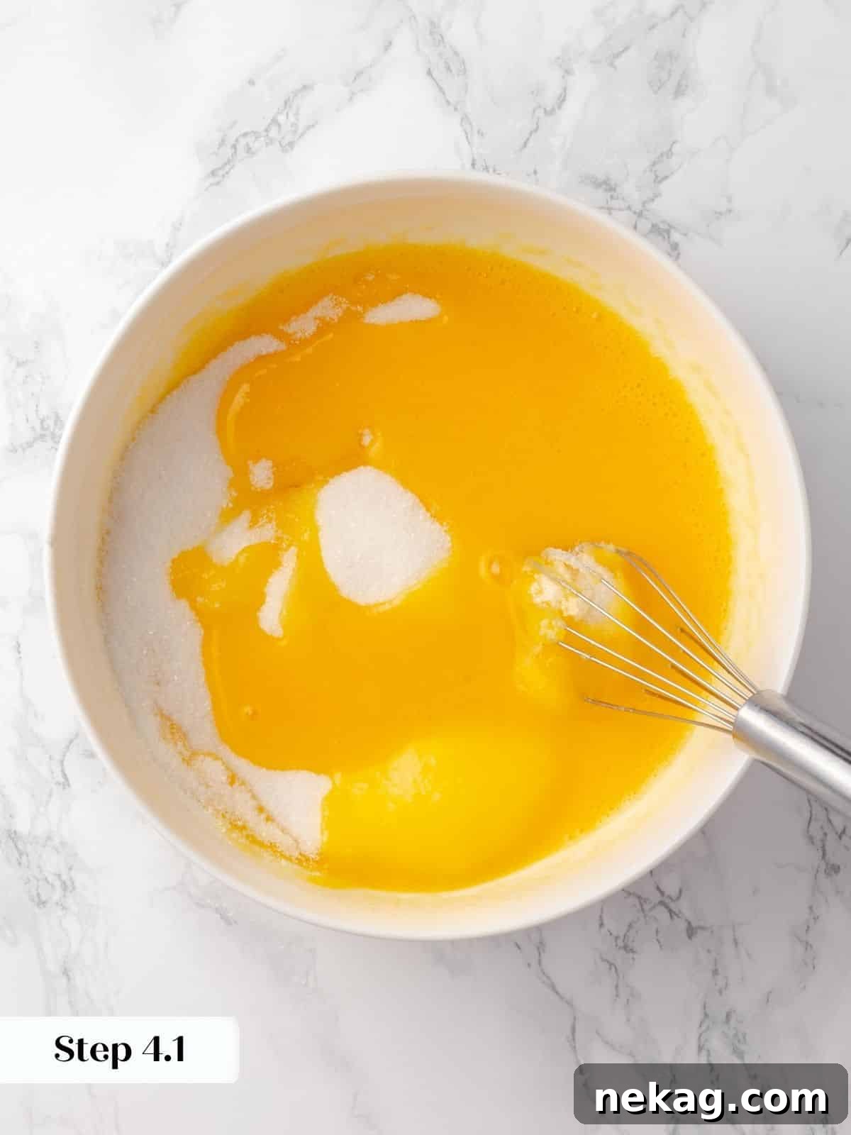 Granulated sugar being added to whisked eggs in a glass mixing bowl, creating a clear visual of the process.