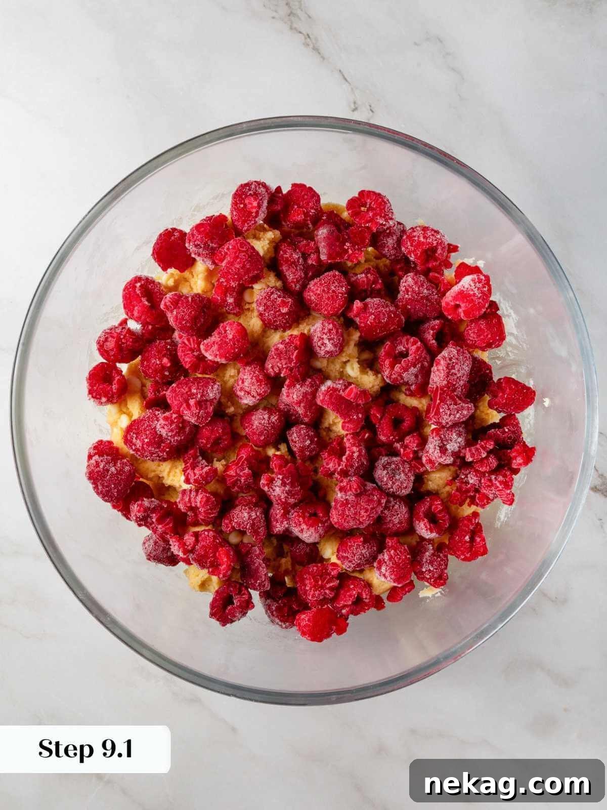 Fresh raspberries being gently folded into the cookie dough to add bursts of fruity flavor.
