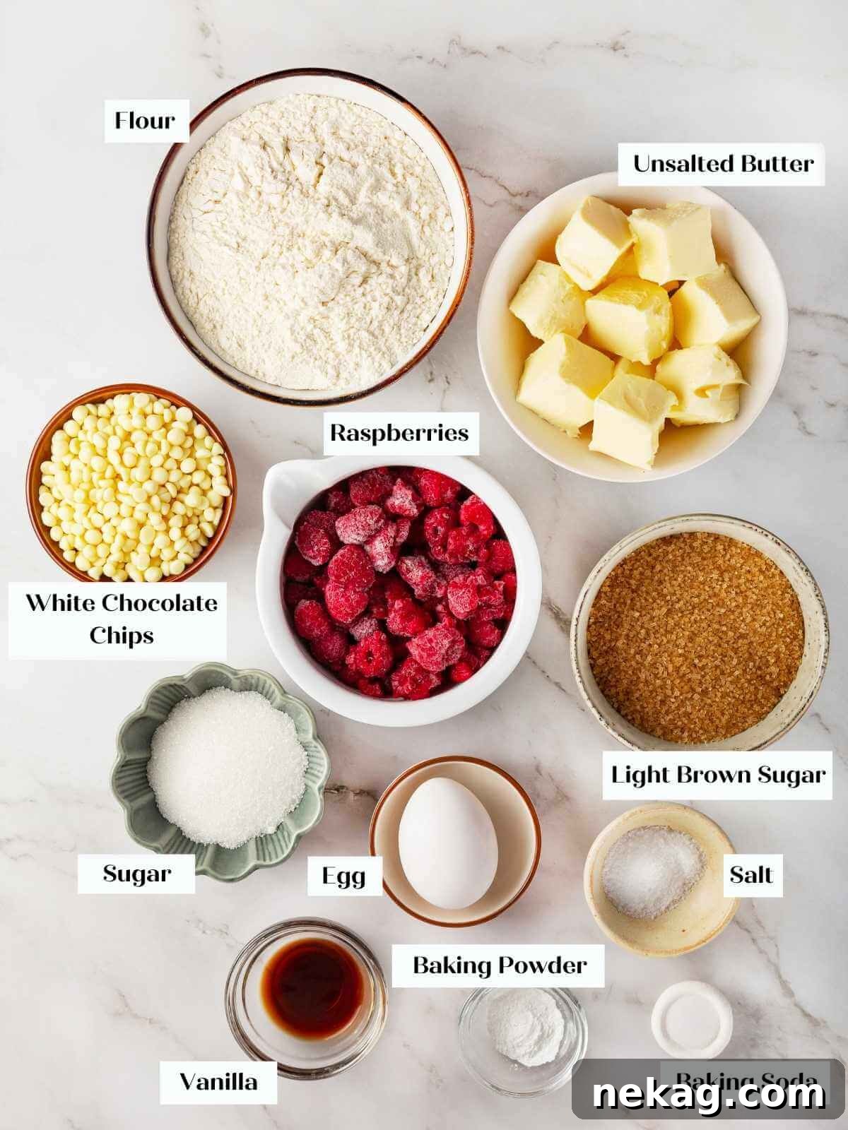Ingredients for white chocolate raspberry cookies, including flour, butter, and fresh raspberries, laid out on a countertop.
