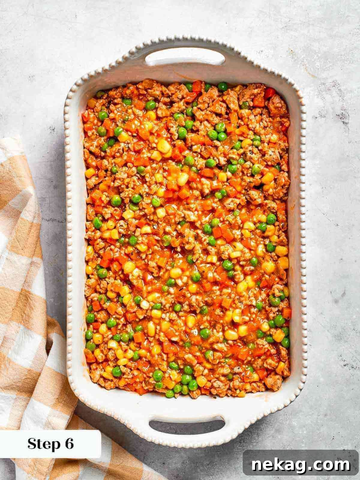 The first layer of Chicken Shepherd’s Pie, a rich and savory ground chicken and vegetable filling, spread evenly in a baking dish before adding the mashed potato topping.
