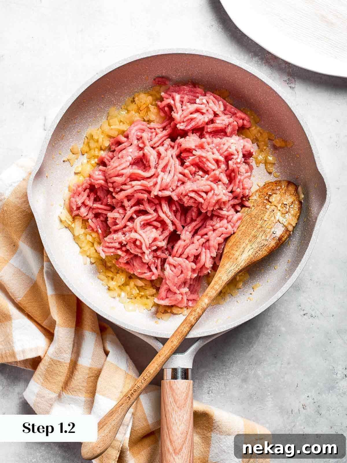 Lean ground chicken being added to a skillet with perfectly sautéed onions and garlic, ready to be browned.