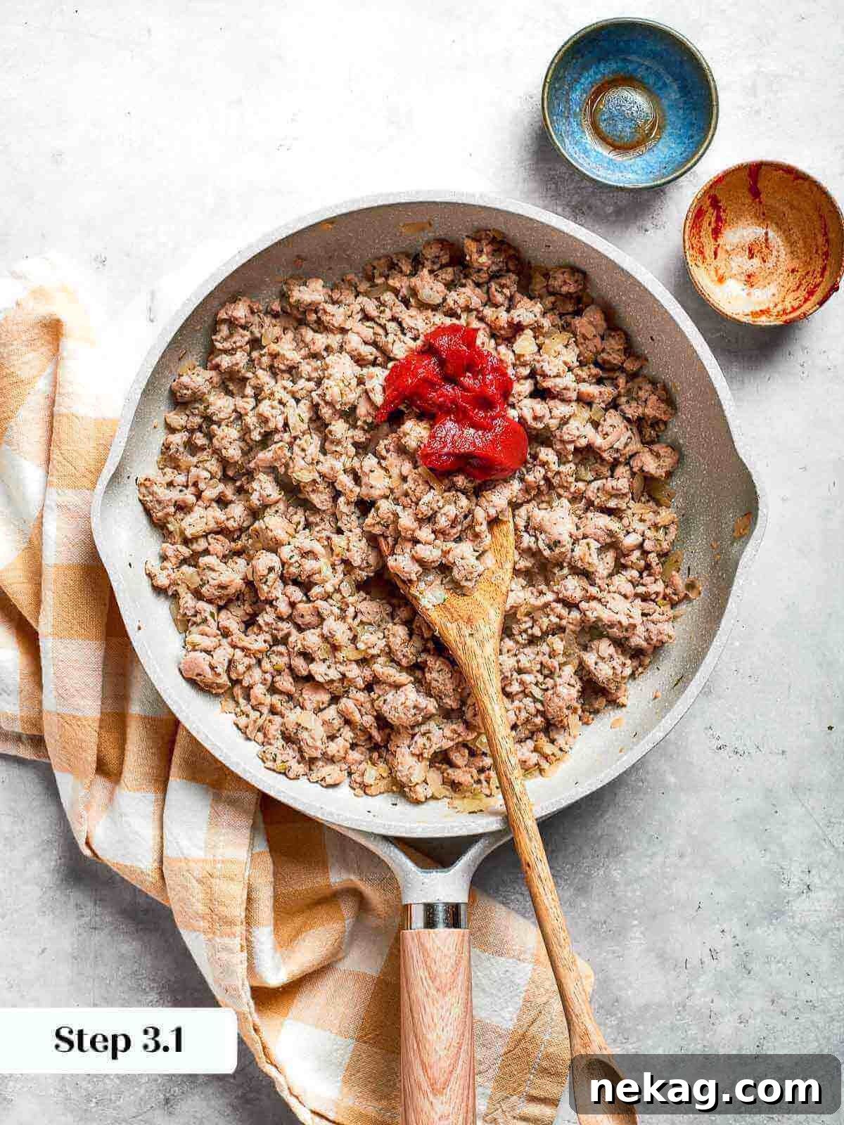A dollop of rich tomato paste being expertly stirred into the savory ground chicken mixture, adding depth and color.