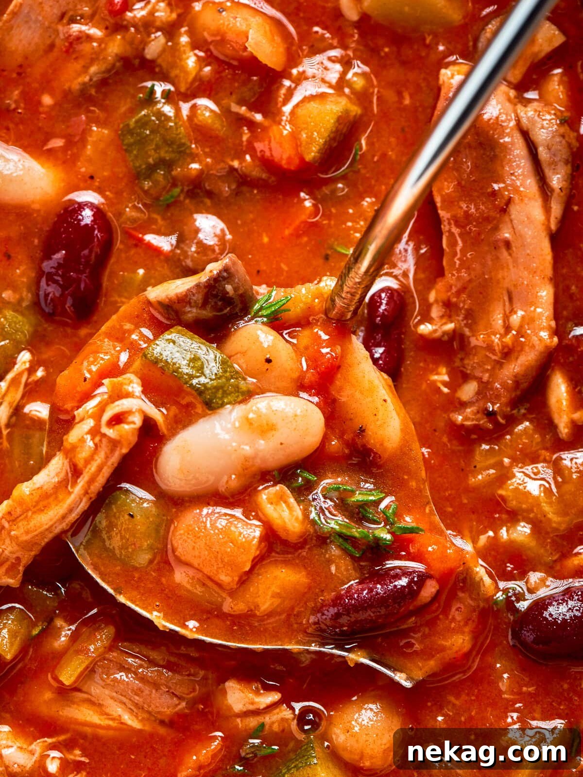 Scooping hot chicken vegetable soup from the pot with a ladle into a serving bowl.
