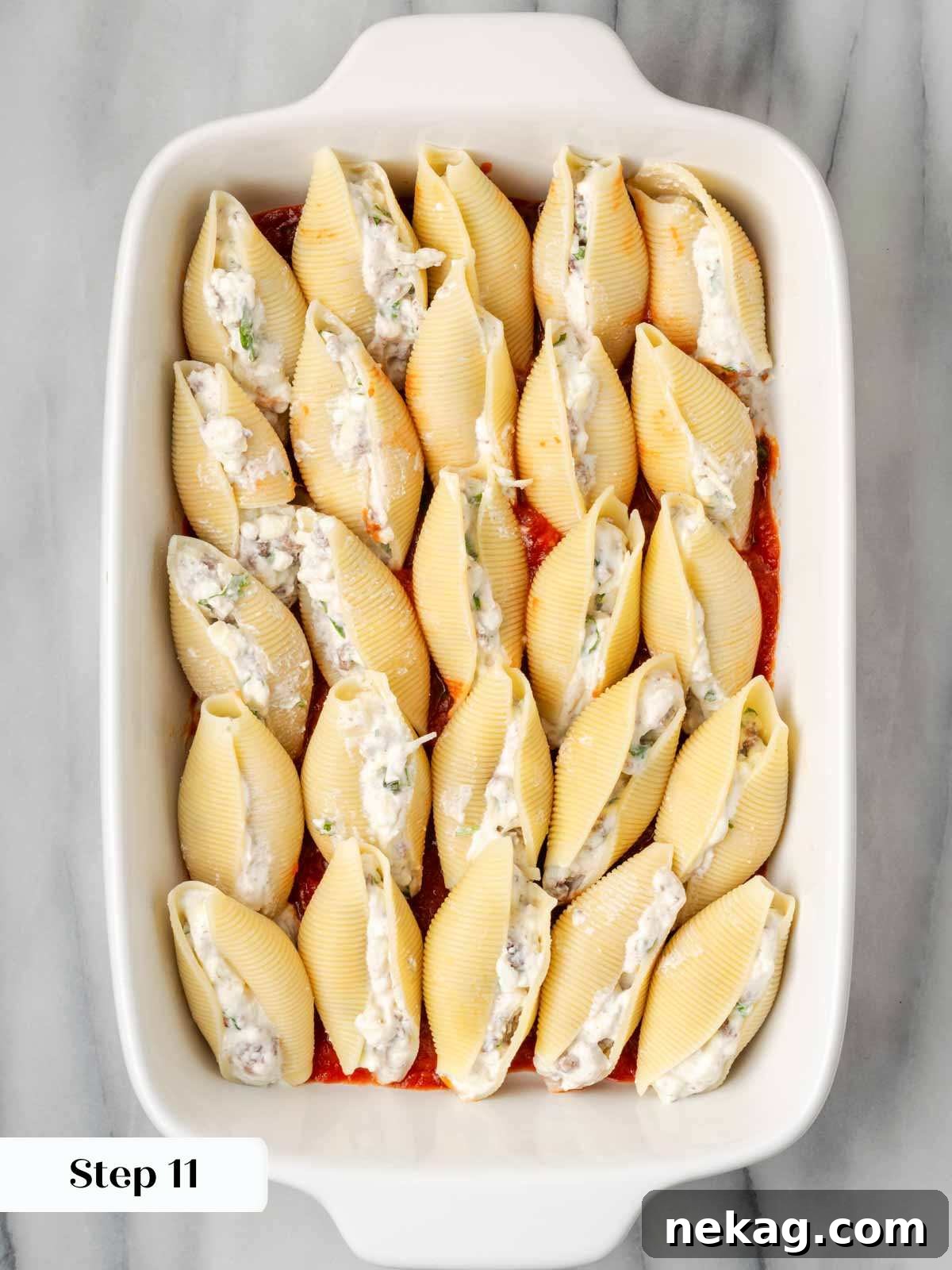 Hearty Meat-Stuffed Pasta Shells 11 Unbaked stuffed shells arranged neatly in a casserole dish, topped with sauce and cheese, ready for the oven.