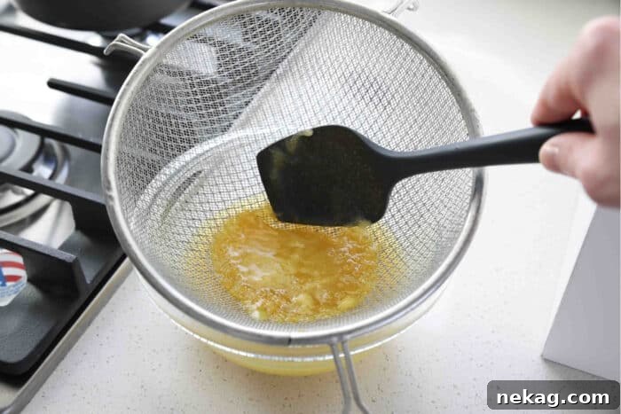 Homemade Lemon Curd Delight 8 Process of straining freshly cooked lemon curd through a fine mesh strainer into a clean bowl for a smooth texture.