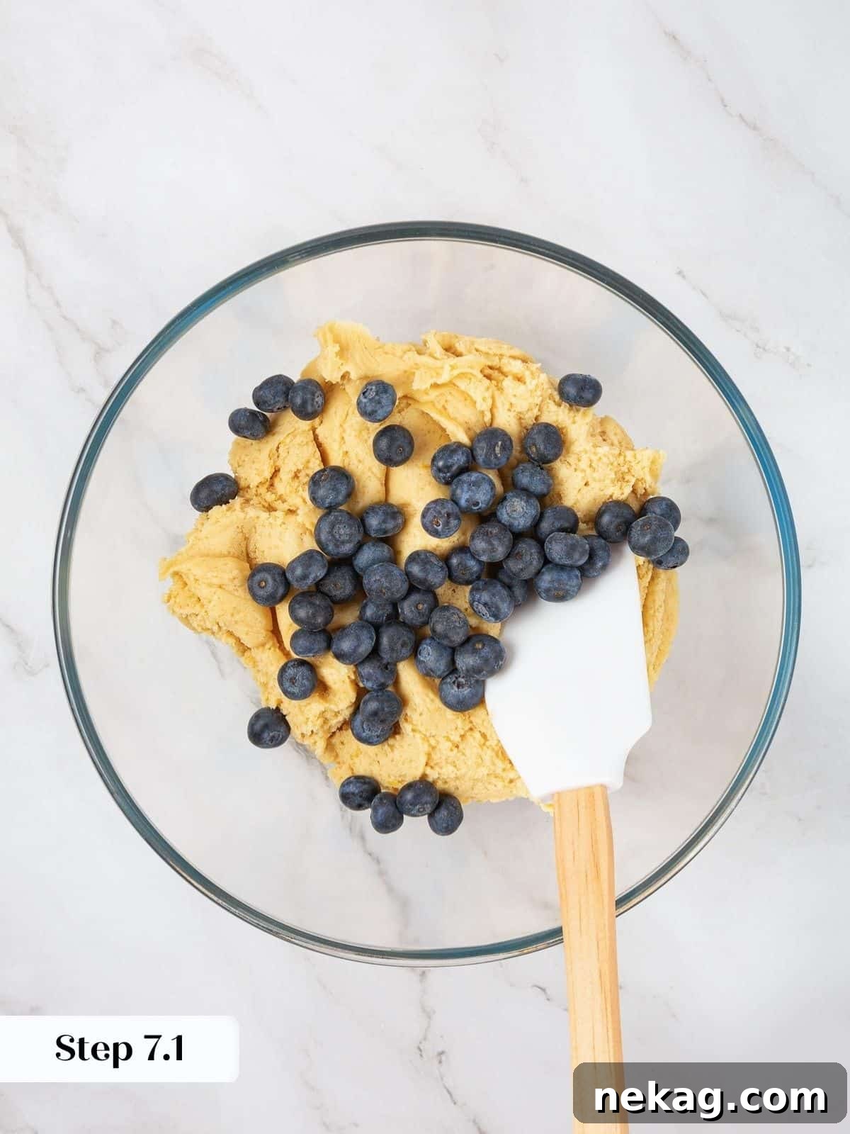 A bowl of lemon cookie dough with fresh blueberries on top, ready to be folded in.