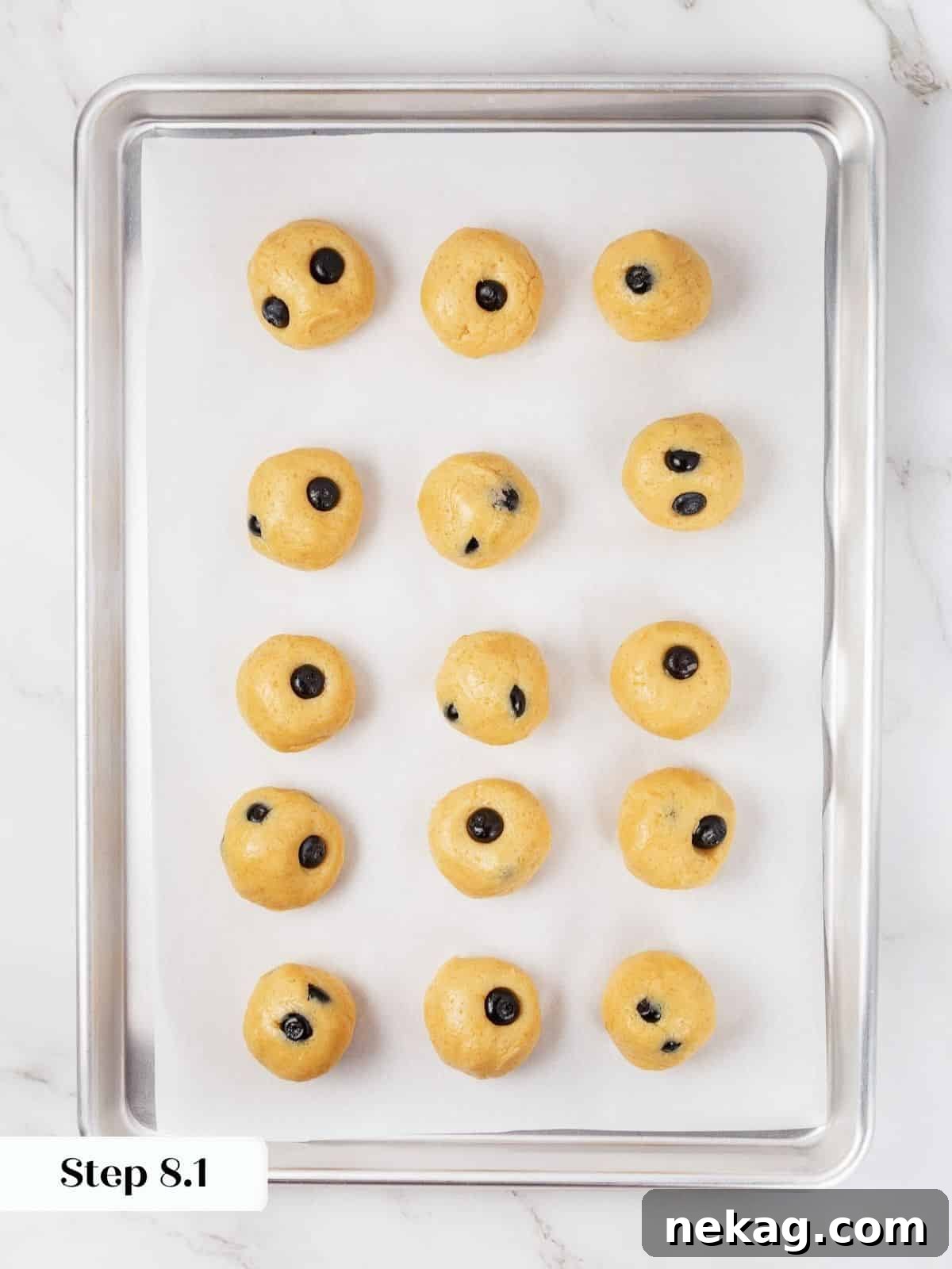 Cookie dough balls lined up neatly on a parchment-lined baking sheet, ready for chilling.