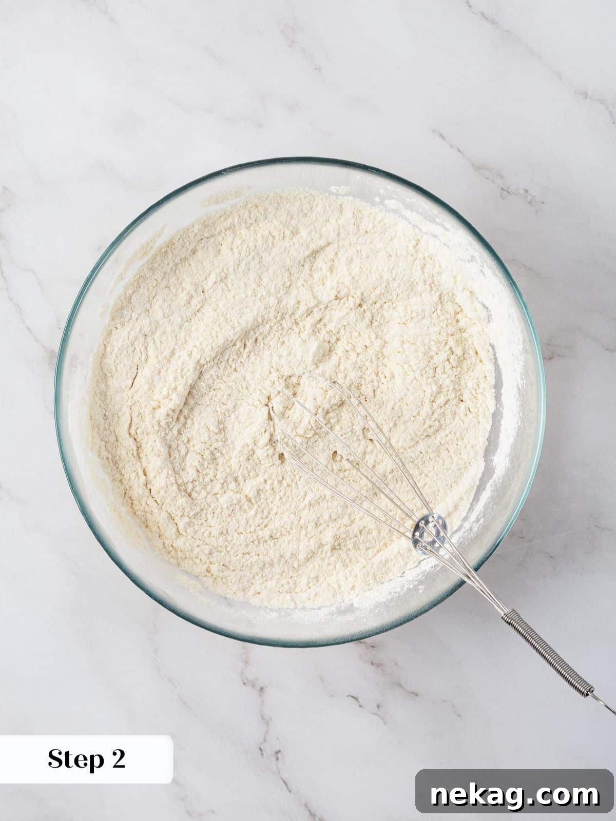 A glass bowl with flour, baking powder, cornstarch, and salt being whisked together.