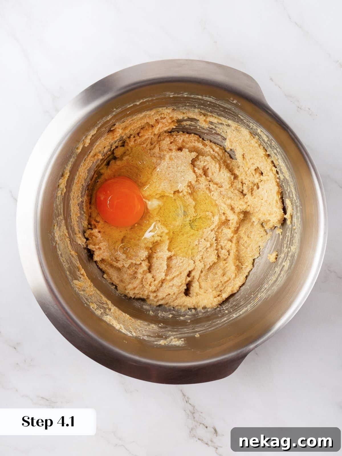 A close-up of an egg just added to the cookie dough mixture, before mixing.