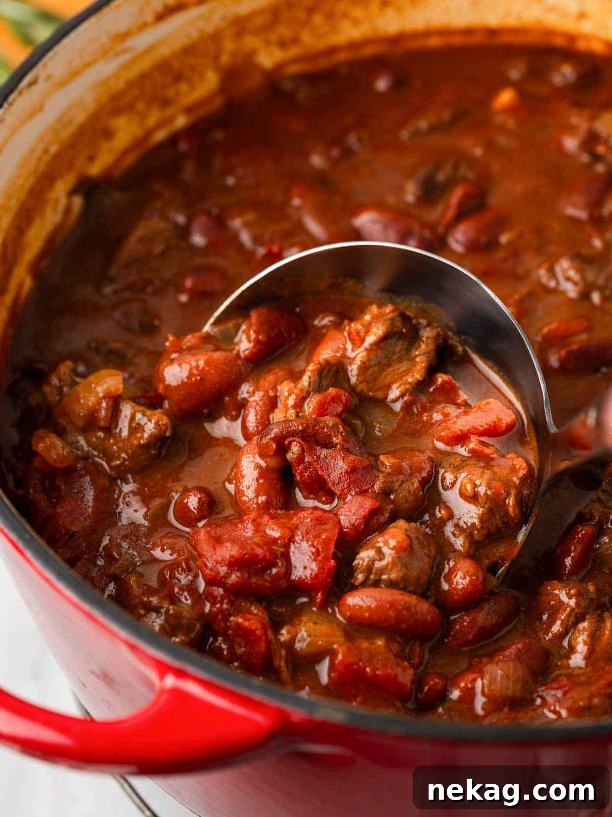 A hearty bowl of rosemary pinot noir steak chili with a ladle, ready to be served, showcasing tender beef, beans, and a rich, dark sauce.