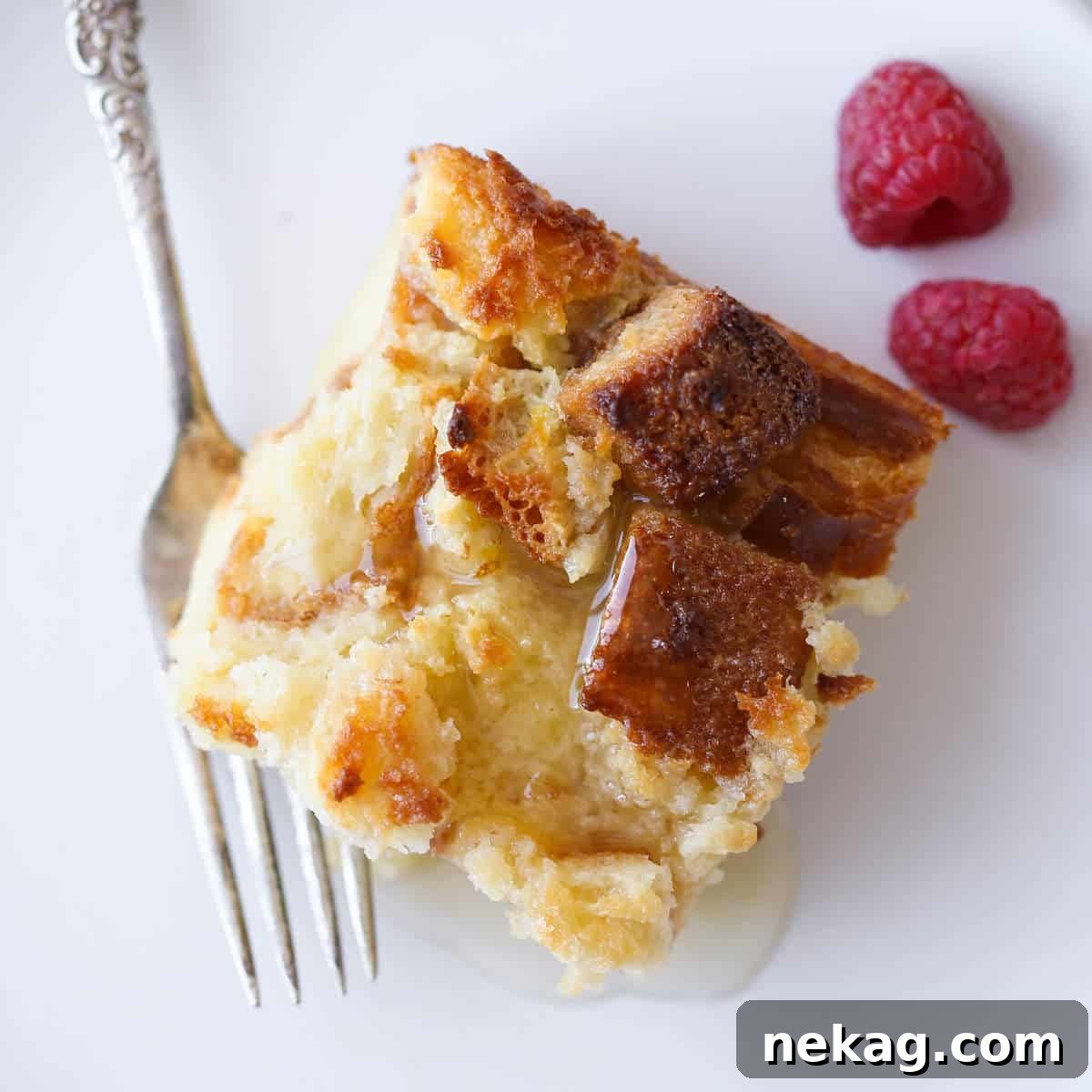 A close-up of a slice of Lemon Raspberry Bread Pudding with fresh raspberries scattered around
