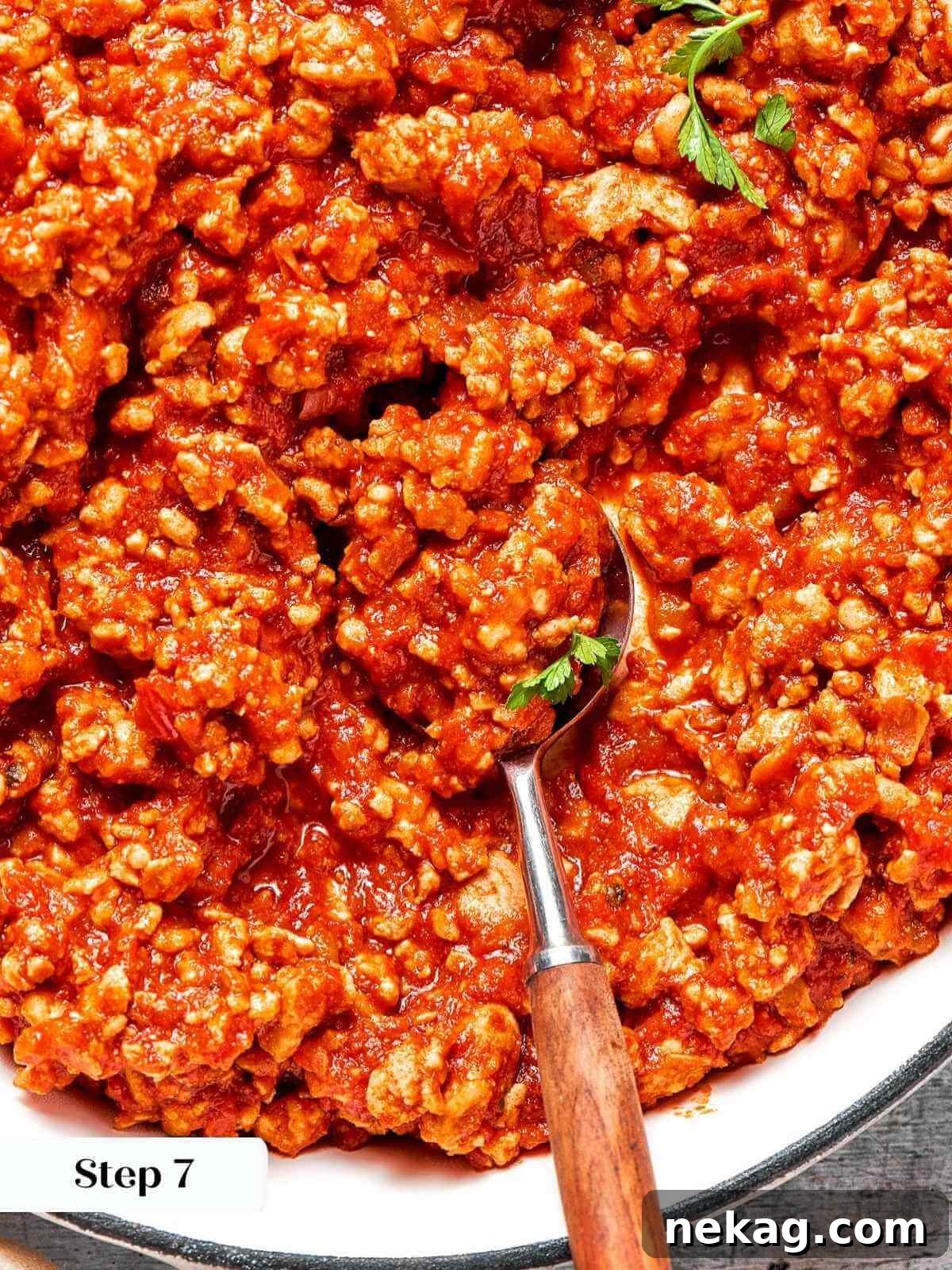 A large serving spoon scooping up the saucy, rich turkey sloppy joe mixture from the pan.