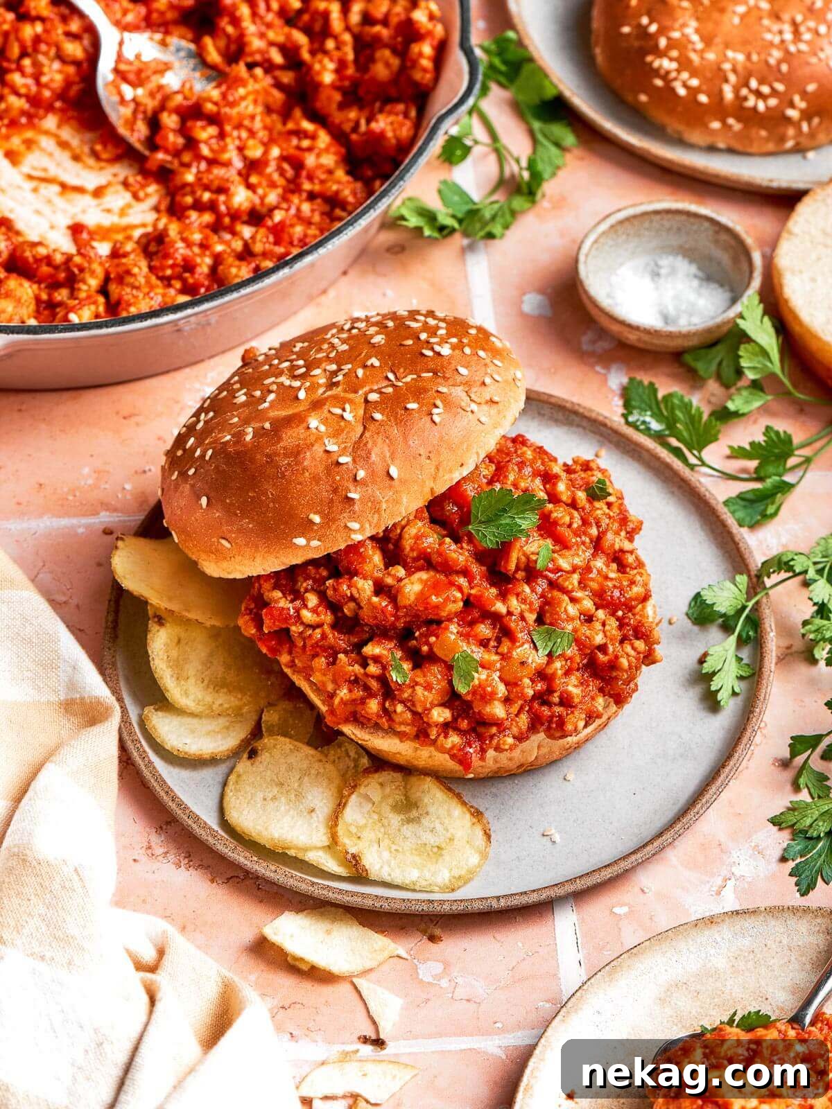A perfectly assembled sloppy joe sandwich plated neatly with a side of crunchy potato chips, ready for a delicious lunch or dinner.