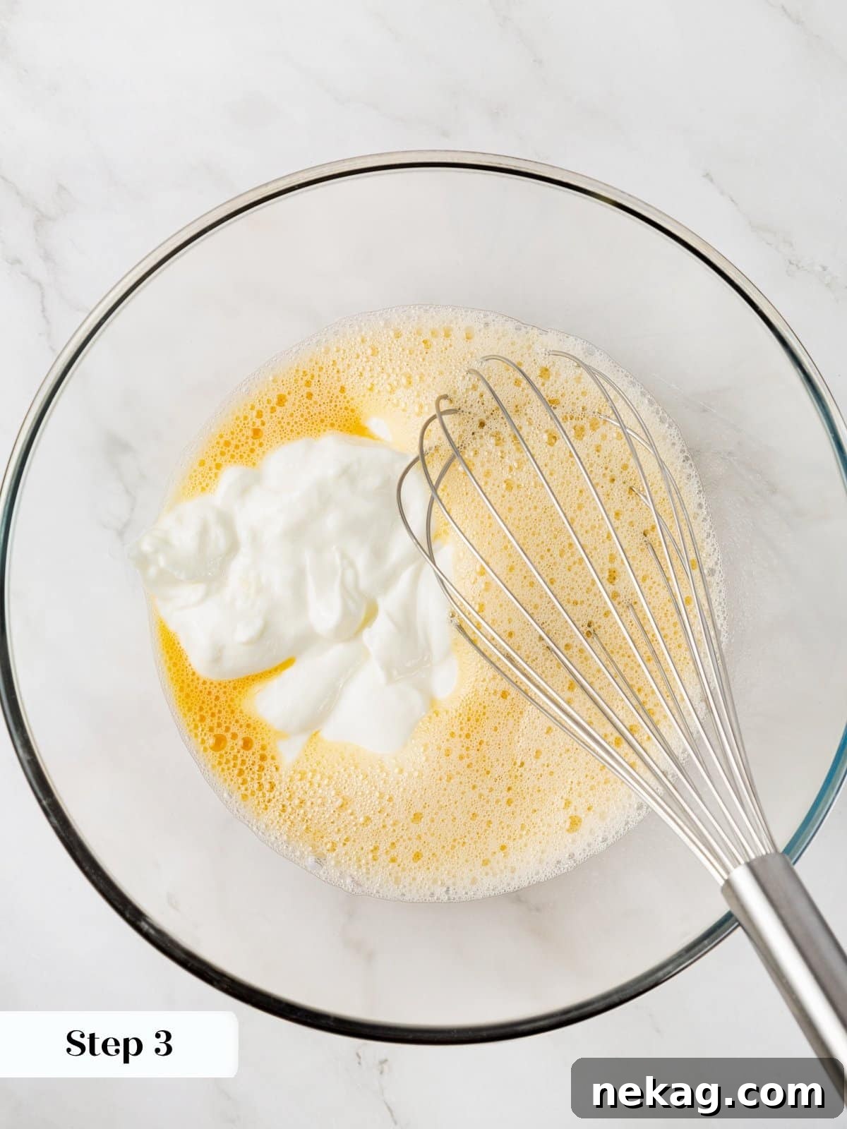 Wet ingredients for healthy carrot muffins, including egg, maple syrup, Greek yogurt, vanilla, and almond milk, being whisked in a clear glass bowl.