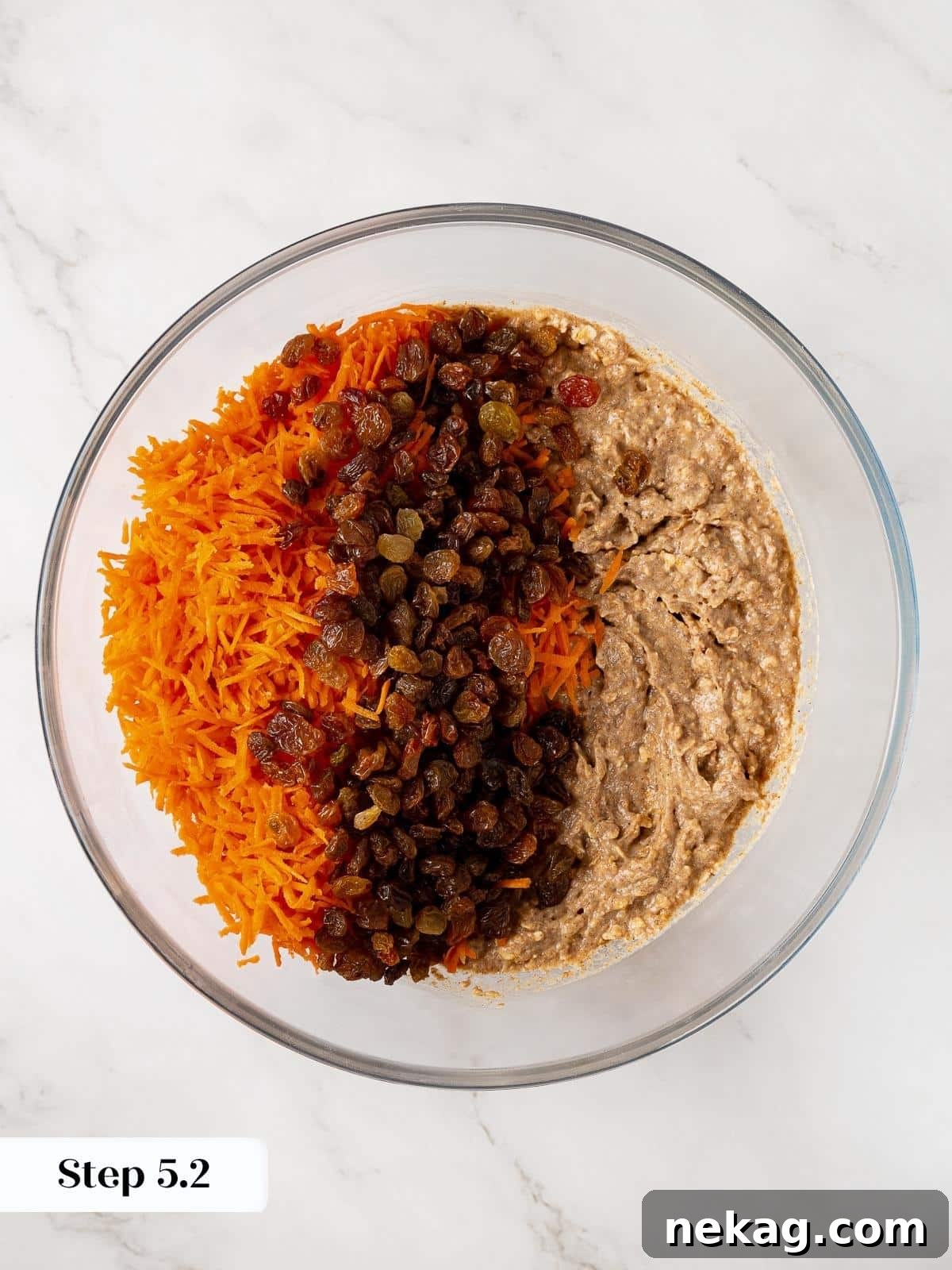 Raisins and grated carrots being carefully folded into the muffin batter using a silicone spatula to prevent overmixing.