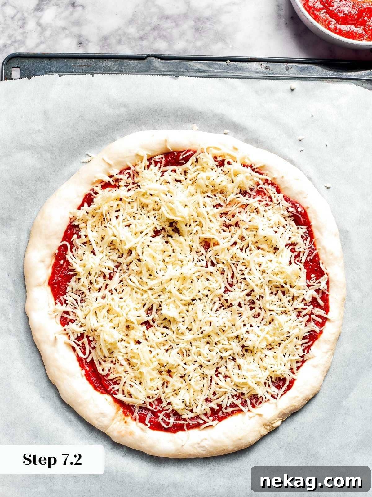 A generous layer of shredded mozzarella cheese evenly distributed on top of the unbaked pizza crust, forming the gooey base.