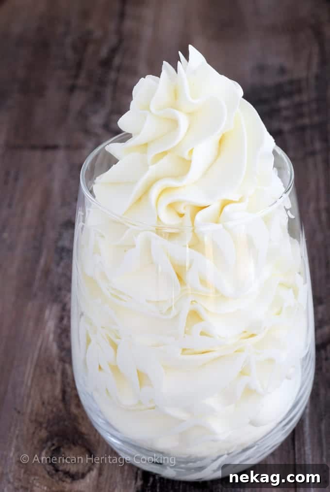 Italian meringue buttercream in a clear glass against a wooden backdrop, showcasing its smooth and airy texture.