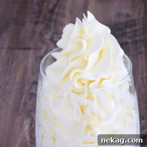 Italian meringue buttercream cleanly piped into a clear glass with a little sticking out of the top.