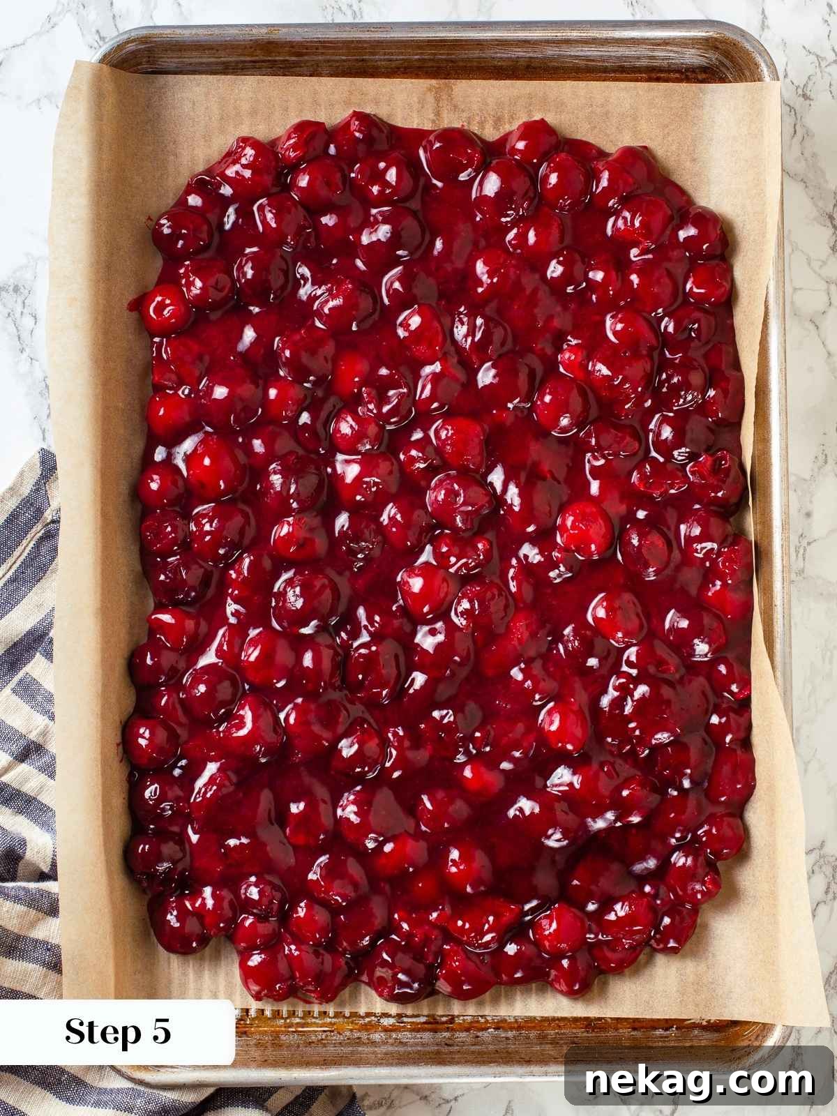 Finished cherry pie filling cooling on parchment-lined baking sheet, deep red and glossy throughout.
