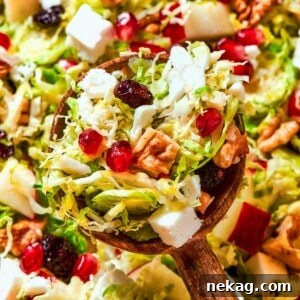 A full spoonful of shaved Brussels sprout salad, showcasing its layered textures and bright, colorful ingredients like sprouts, pears, cherries, and feta.