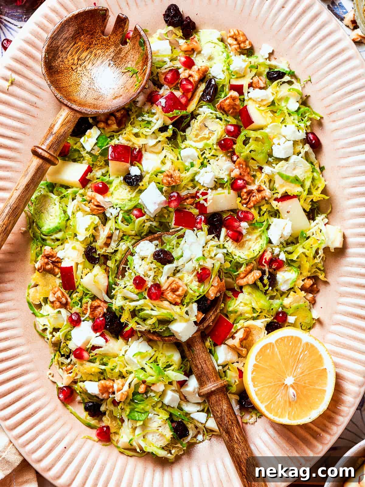 A freshly sliced lemon half rests beside a vibrant bowl of finished shredded Brussels sprouts salad, emphasizing the fresh ingredients.