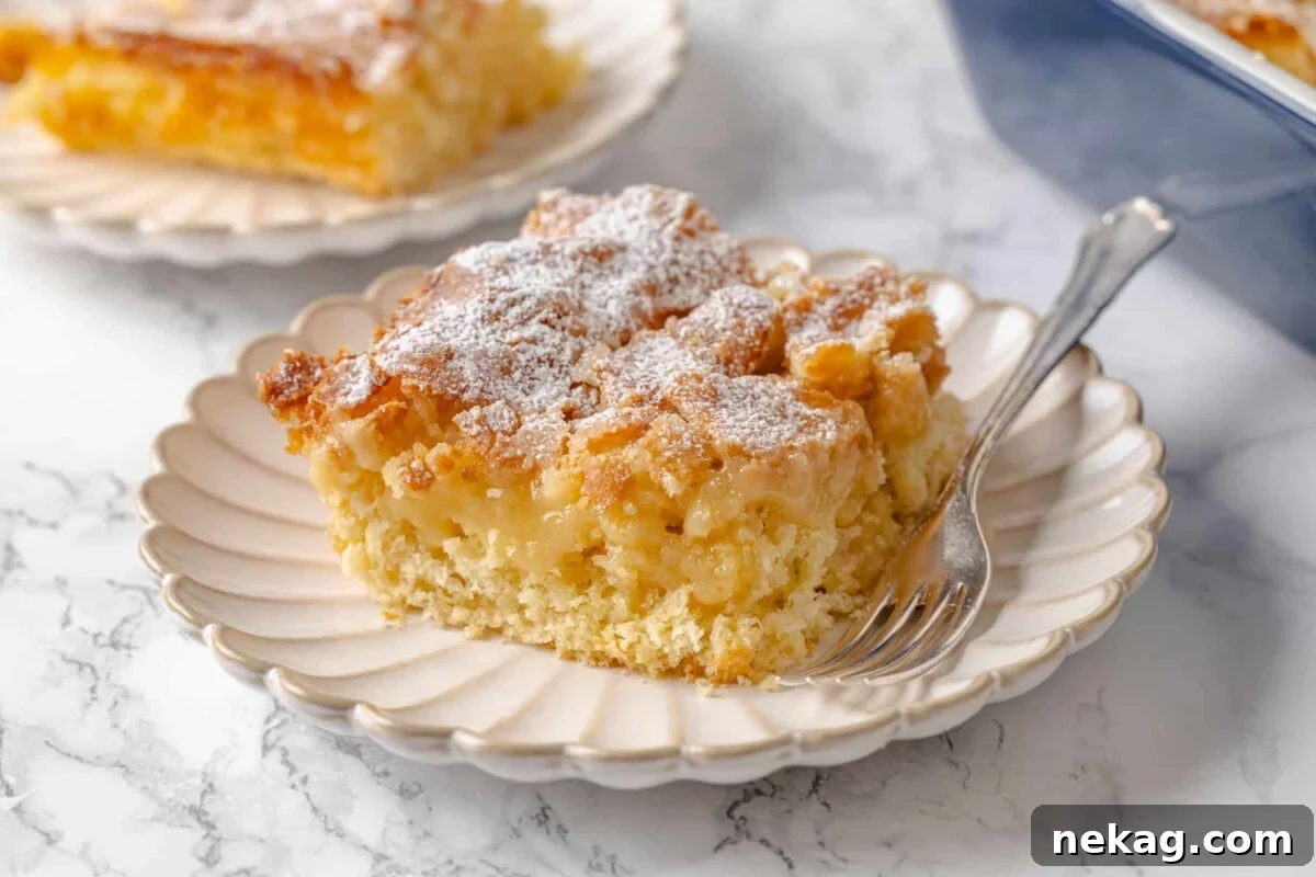 A fork by a piece of gooey butter cake showing distinct layers of golden crust and a soft, luscious filling.