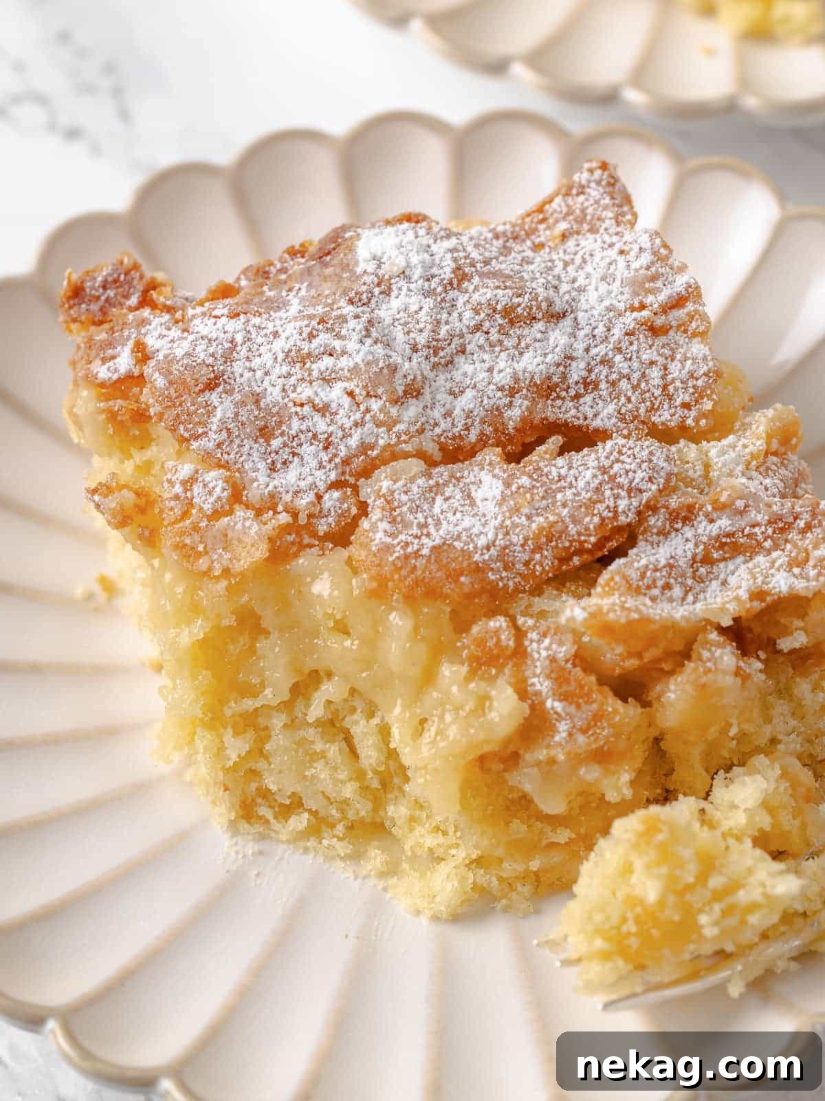 A single, delectable slice of gooey butter cake with a bite taken, revealing its incredibly soft texture and moist, luscious center.