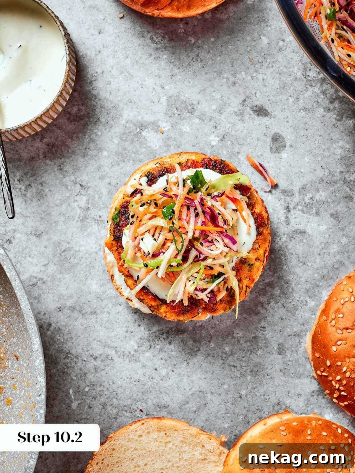 Assembled burger with top bun off showing layers of salmon, slaw, and sauce.