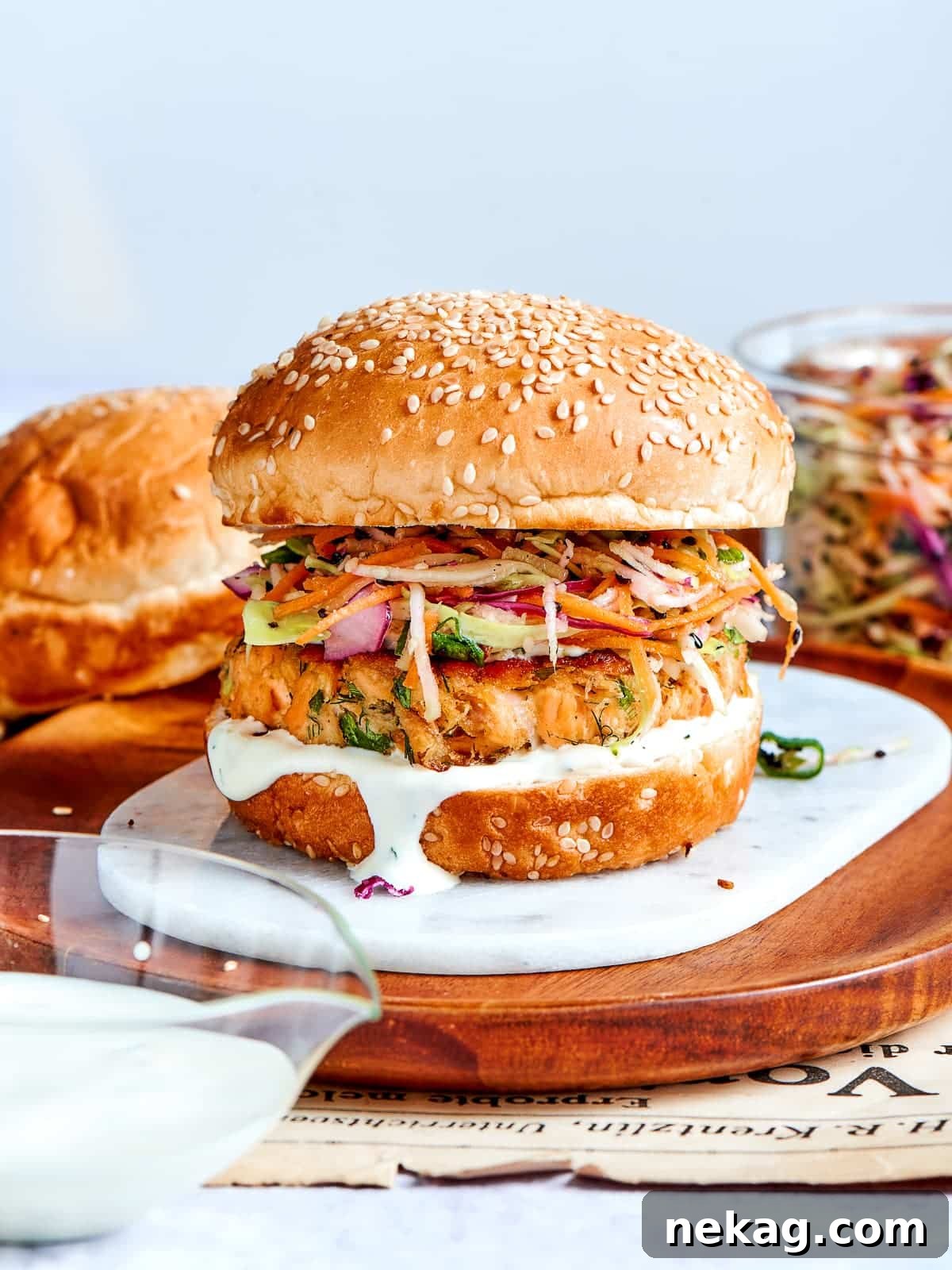 Salmon burger topped with sesame bun, served on wood with slaw spilling out.